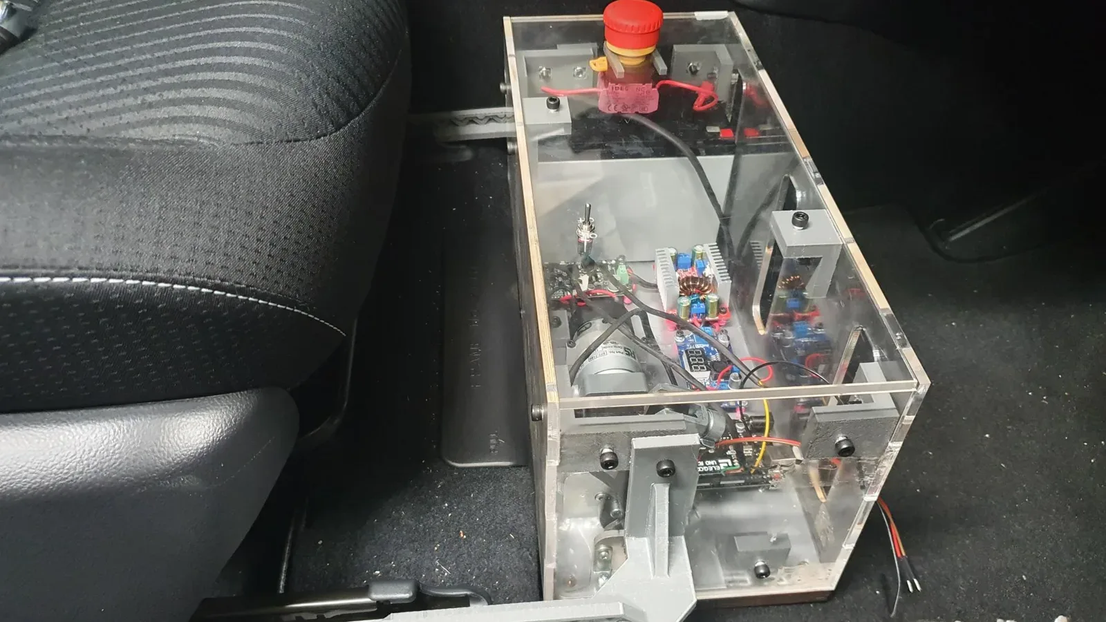 The robot installed in the footwell of the test car, a Prius plug-in hybrid: the acrylic enclosure fixed to its baseplate with the output arm reaching down towards the pedal.