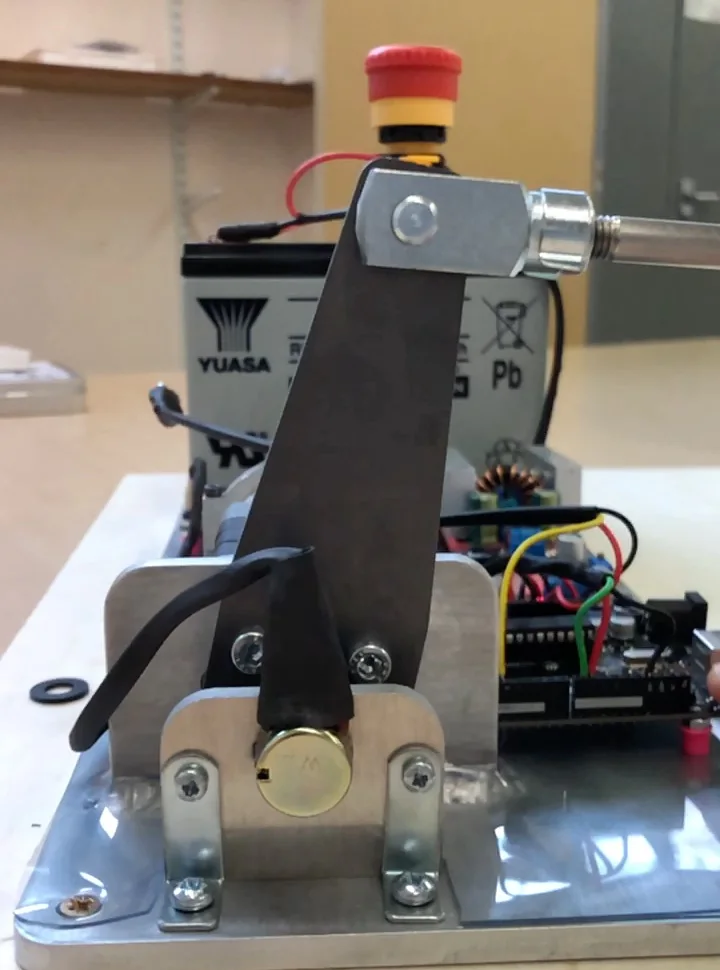 The pedal robot as built: the actuator arm rising from its baseplate with an emergency stop on top and a battery behind