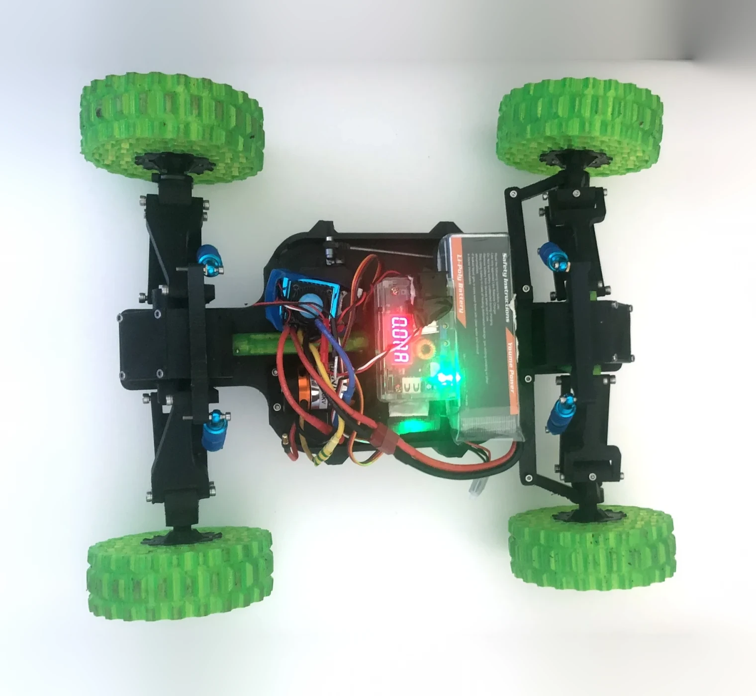 Plan view of a four-wheeled rover with green 3D-printed tyres, powered up, with a battery and current meter visible