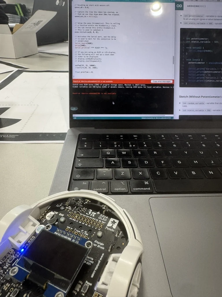 A Pololu 3Pi+ 32U4 robot on a lab bench in front of a laptop showing the Arduino IDE, with the sketch open and a board-not-available error in the console.