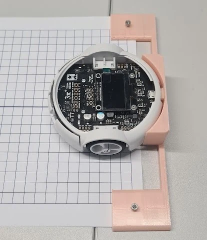The robot held in a 3D-printed alignment jig on graph paper, the jig bracketing the wheels so the robot starts square to the printed grid.