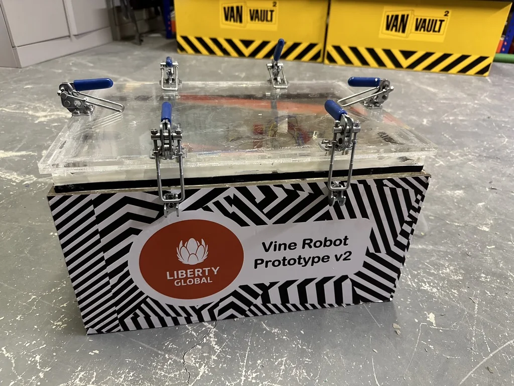 The second vine robot prototype: an acrylic lid held down by steel toggle clamps onto a vinyl-wrapped body carrying a Liberty Global logo and the label Vine Robot Prototype v2