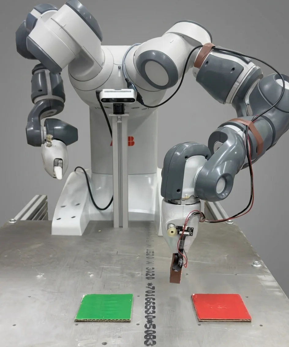 An ABB YuMi dual-arm robot at a steel work table. A RealSense camera is mounted on its chest and a 3D-printed optical tactile sensor is fitted in place of the left gripper. A green square and a red square sit on the table in front of it.