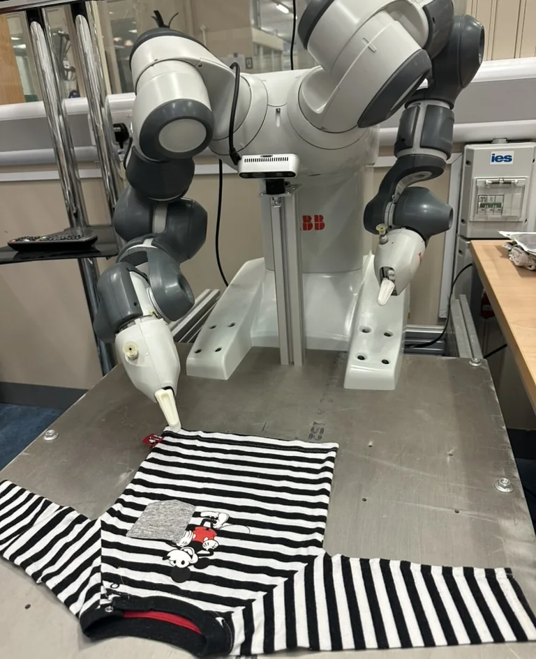 An ABB YuMi dual-arm robot at a work table with a striped child's top laid out in front of it